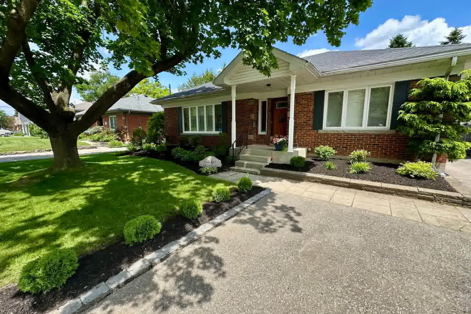 Well-maintained front yard with neat lawn, shaped shrubs, mulched beds and a clean walkway at a Brantford home.
