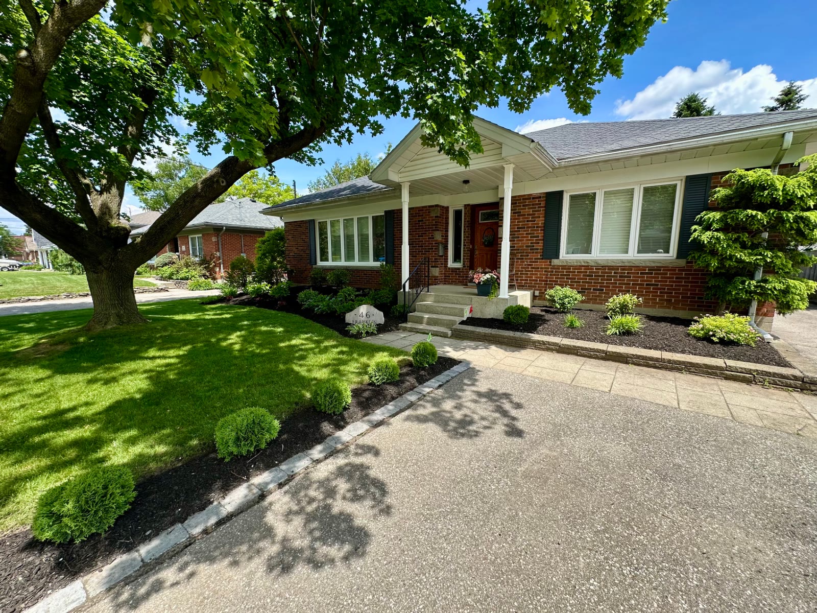 Front yard with a stone-edged cedar border along the driveway, mulched beds and a freshly cut lawn under a maple tree.