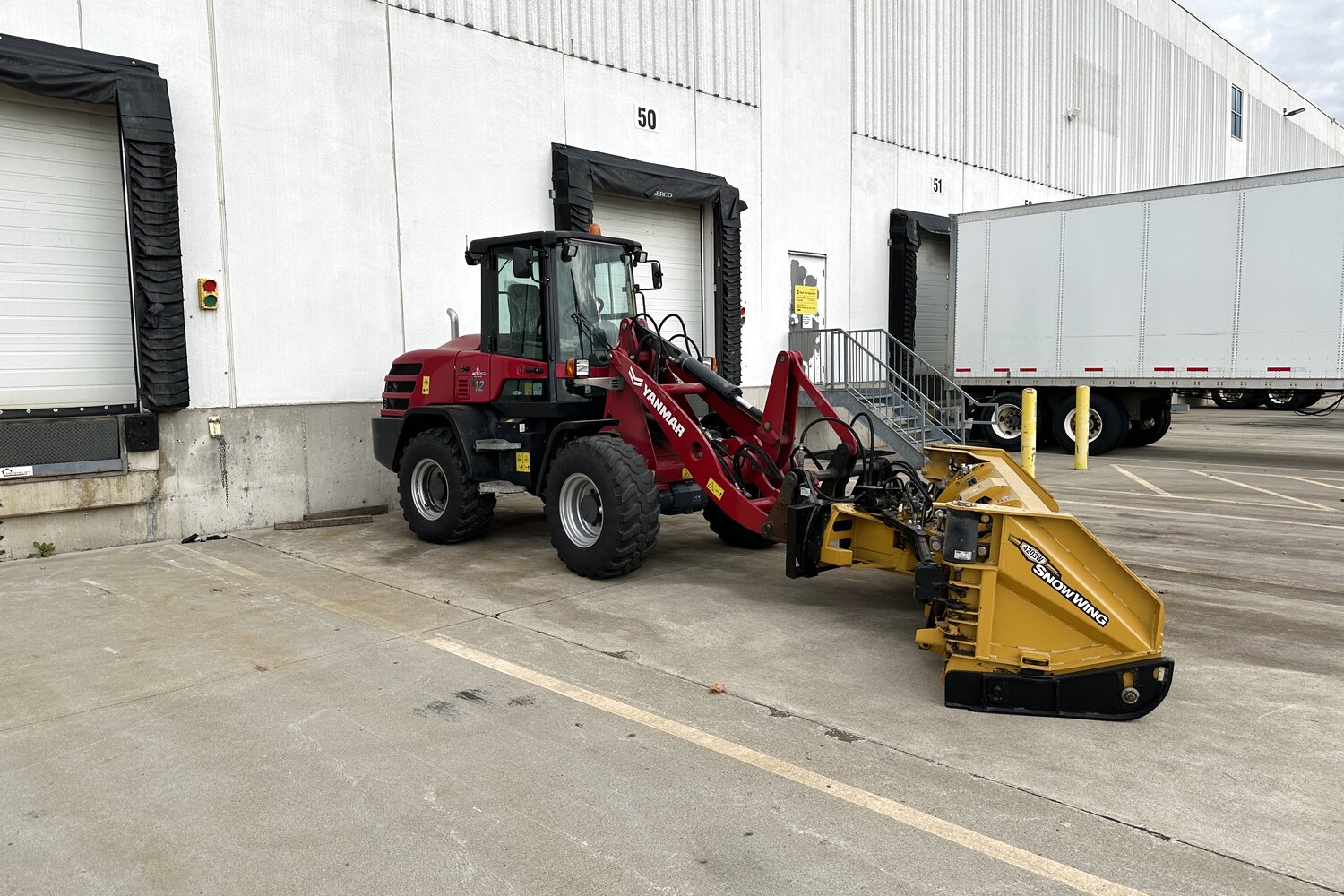 Red Yanmar wheel loader with a yellow SnowWing pusher clearing a commercial parking lot in Brantford.