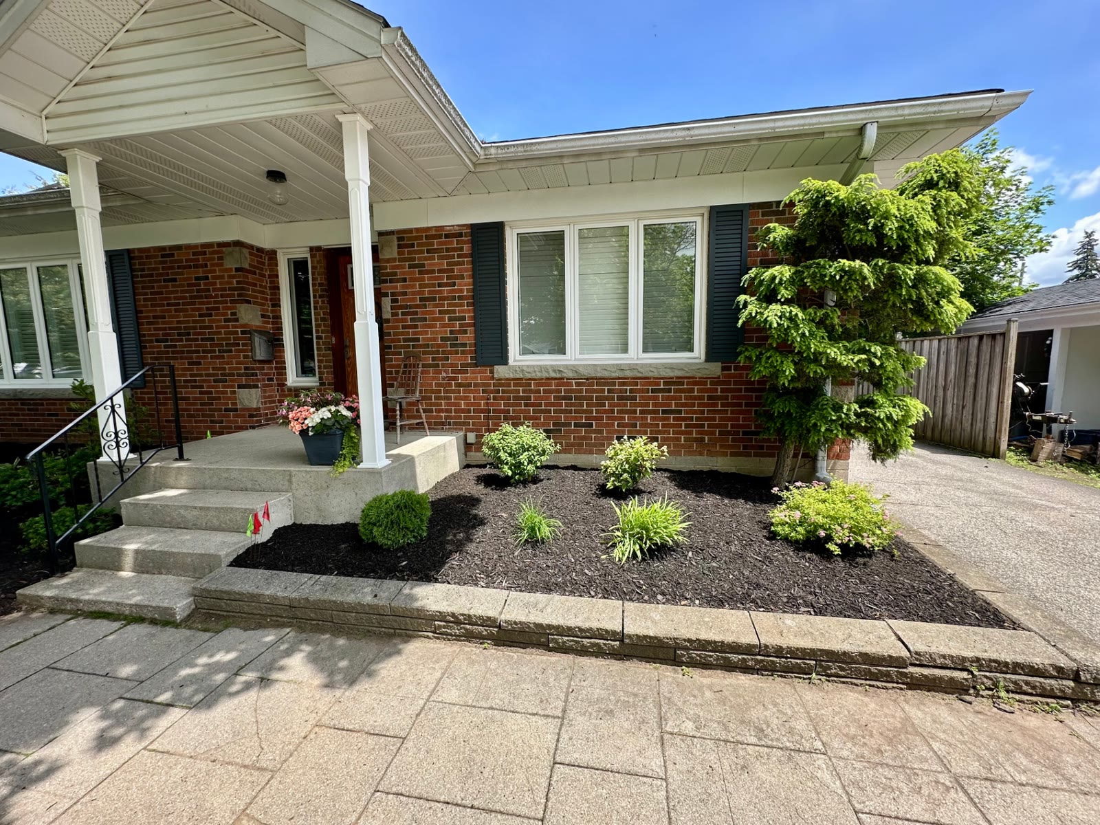 Bed along a driveway and front porch planted with small shrubs and grasses in fresh mulch.