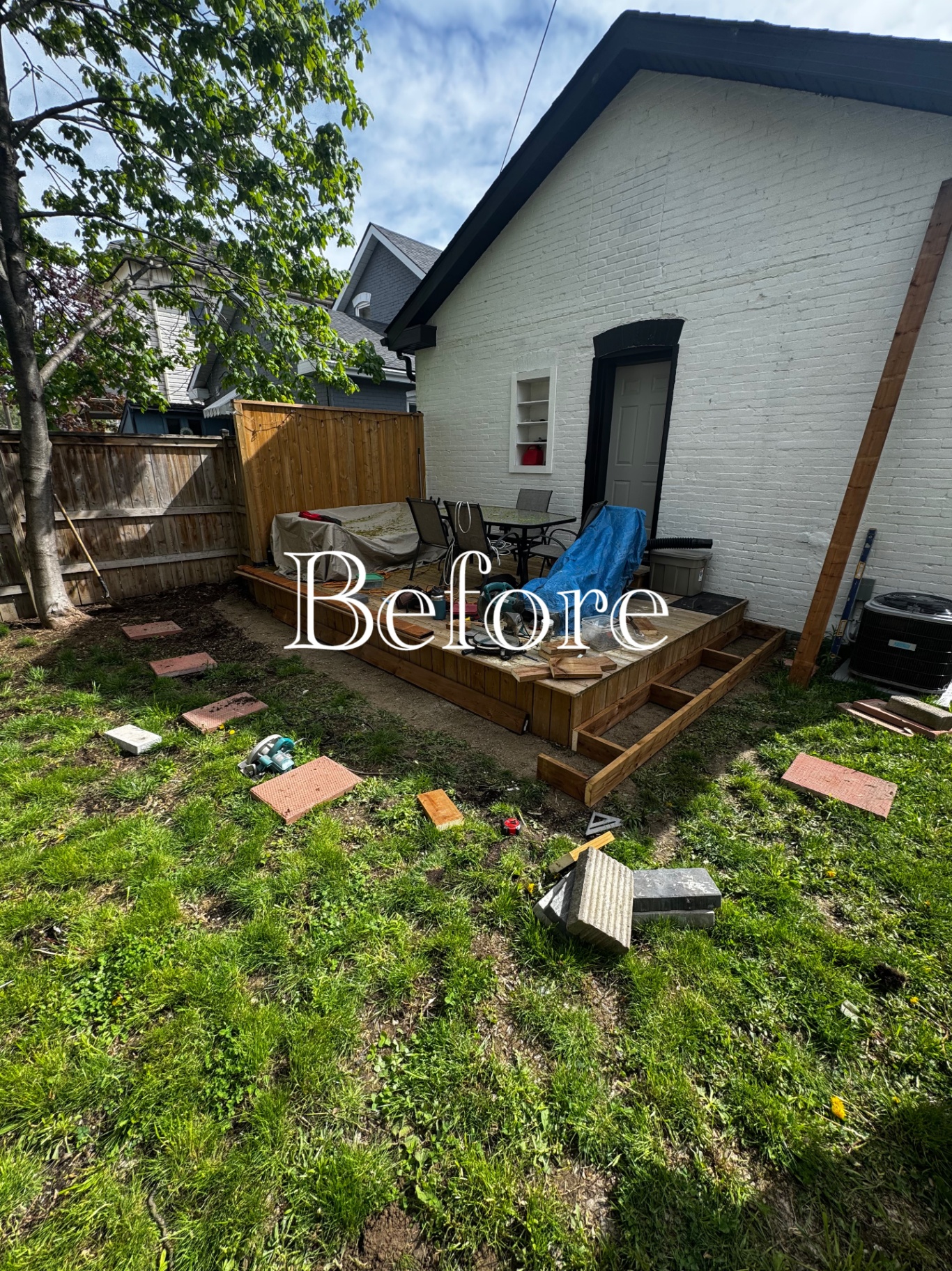 Backyard deck and lawn before a patio build, with pavers and tools staged on site.