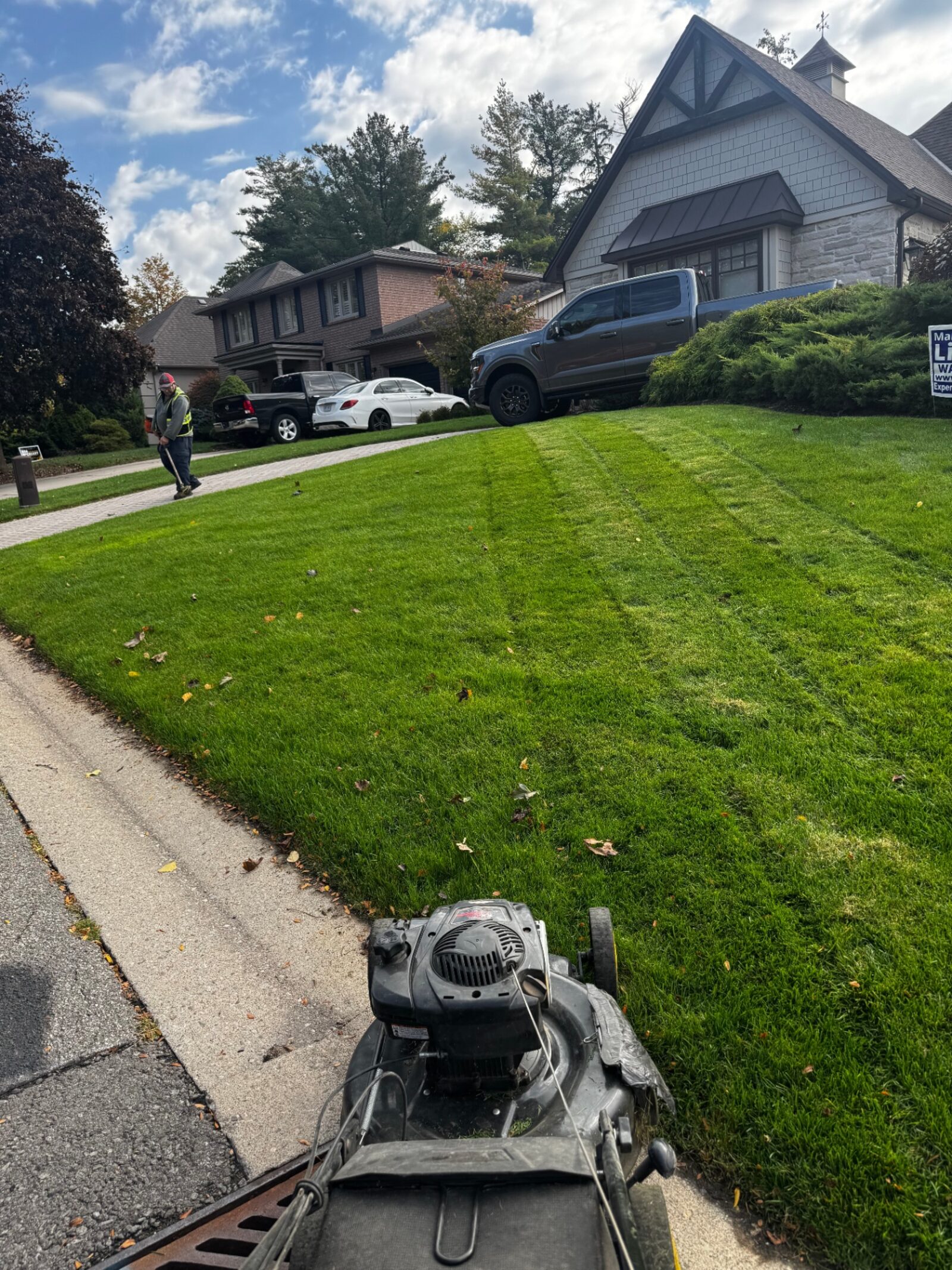 Crew member mowing a residential front lawn with a push mower in Brantford, Ontario.