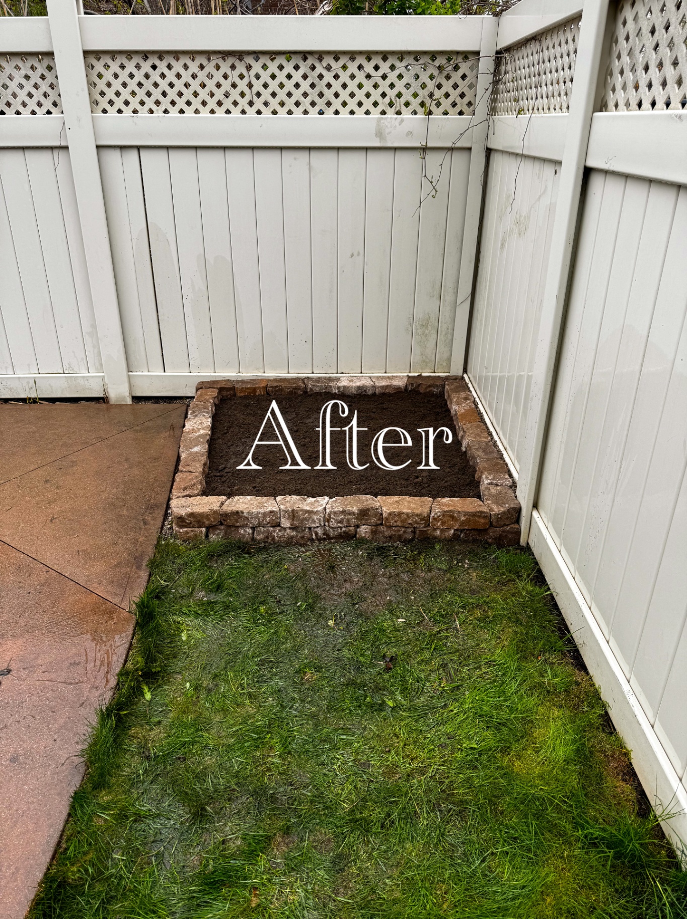New stone-edged raised garden bed filled with fresh soil in a fenced yard corner.