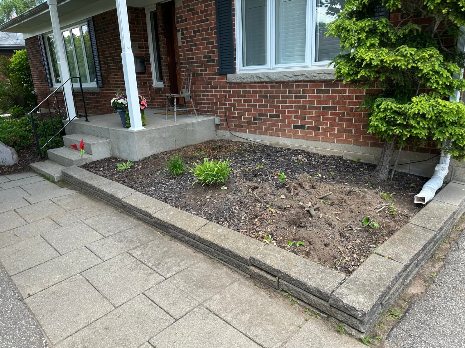 Stone-edged front porch bed before planting, with bare soil, old mulch and only a few remaining perennials.