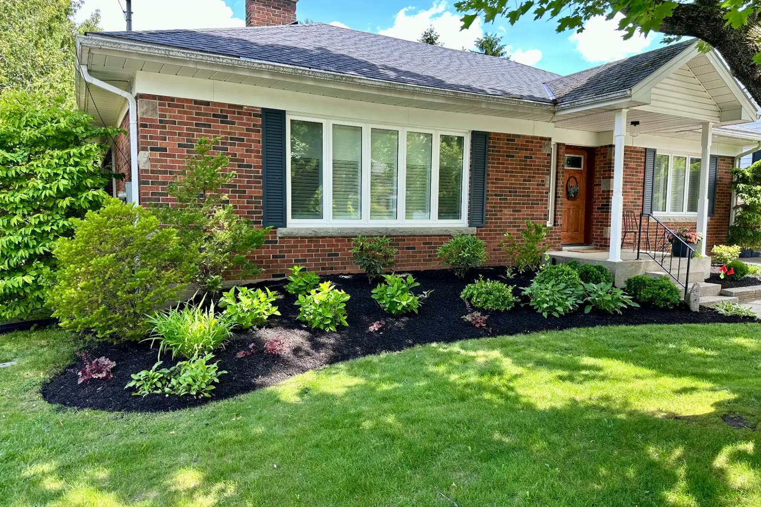 Brick bungalow in Brantford with fresh black mulch, hostas, shrubs and a neat lawn edge along the foundation beds.