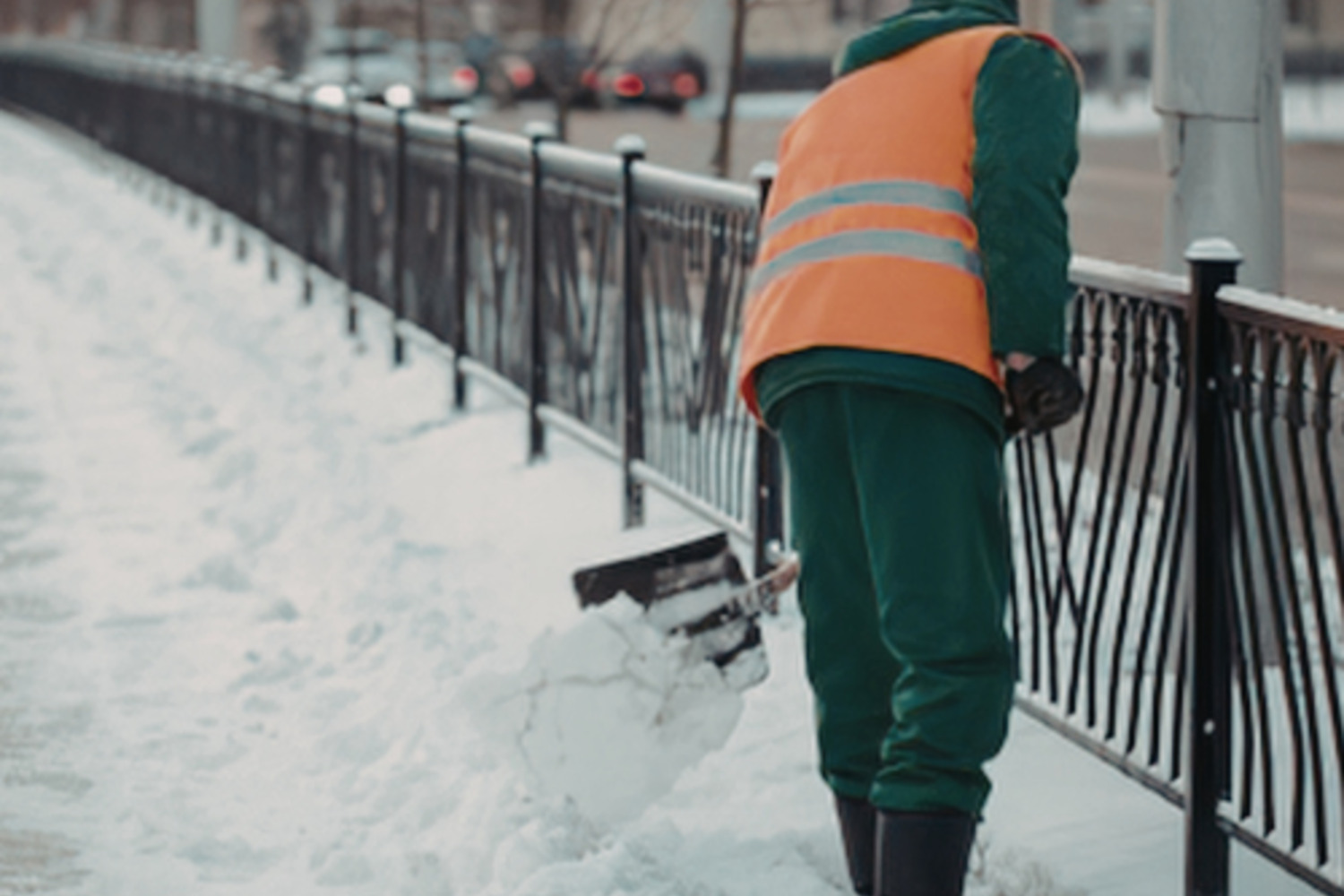 Crew member shovelling a snow-covered sidewalk beside a railing at a Brantford property.