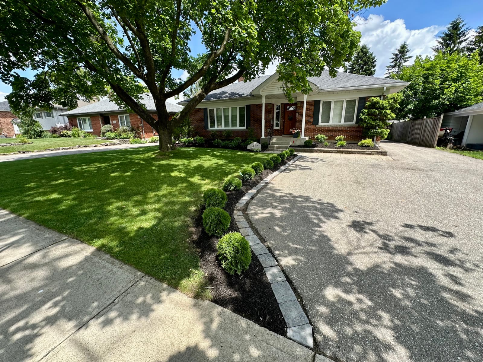 Wide view of a finished front yard with a curved stone-edged cedar bed, mulched foundation beds and healthy lawn.